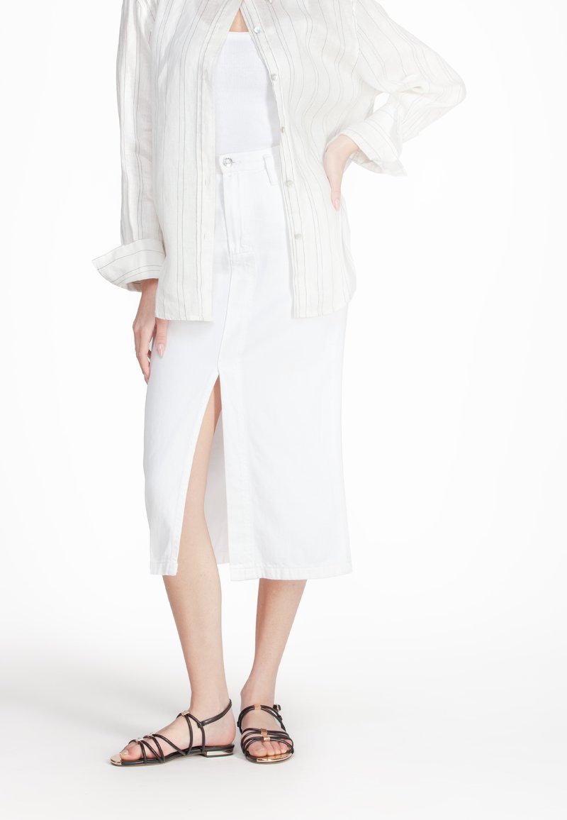 Gonna midi bianca in cotone con spacco frontale, abbinata a una camicia button-up beige a righe e sandali neri con cinturini. Tessuto morbido e design casual.