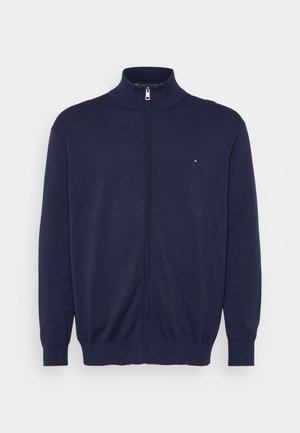 Donkerblauwe ritstrui met hoge kraag, lange mouwen, ribgebreide boorden en zoom, met een klein logo op de linkerkant van de borst. Zachte textuur.