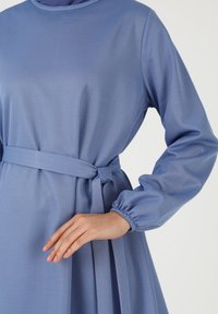 Hellblaues Kleid mit langen Ärmeln und einem taillierten Bund. Texturiertes Gewebe mit einem subtilen Muster, das geraffte Manschetten aufweist.