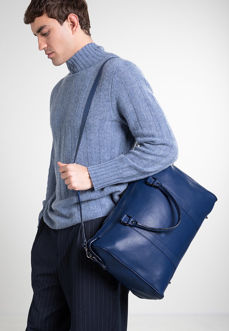 Dunkelblaues Leder-Duffle-Bag mit einer strukturierten Form, texturiertem Finish, doppelten Griffen und einem abnehmbaren Schultergurt.