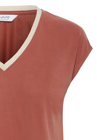 Košile s krátkými rukávy v barvě rezavé s béžovým lemováním véčkového výstřihu, viditelná etiketa uvnitř límce, hladká textura látky.