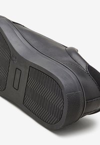 Čierne slip-on topánky s hladkým koženým vrchom, štruktúrovanou gumovou podrážkou so zigzagovým vzorom a minimalistickým dizajnom.