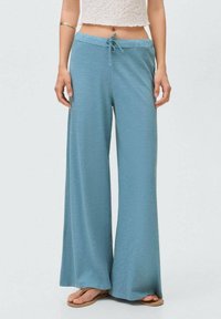Light blue wide-leg trousers made of soft fabric with an elastic waistband and drawstring detail, paired with a white cropped top.