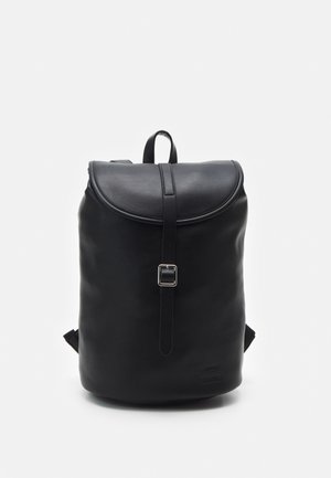 Sac à dos en cuir noir avec fermeture à rabat et sangle avant à boucle, posé debout sur fond blanc.