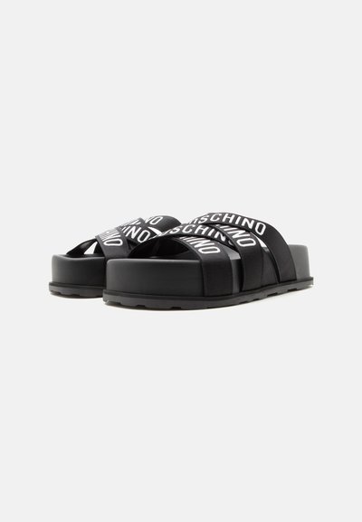 Sandales plates-formes noires avec des sangles épaisses croisées affichant un logo en texte blanc.
