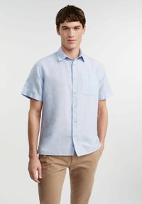Koszula z krótkim rękawem, jasnoniebieska, zapinana na guziki, wykonana z przewiewnego materiału, z kieszonką na piersi i luźnym krojem.