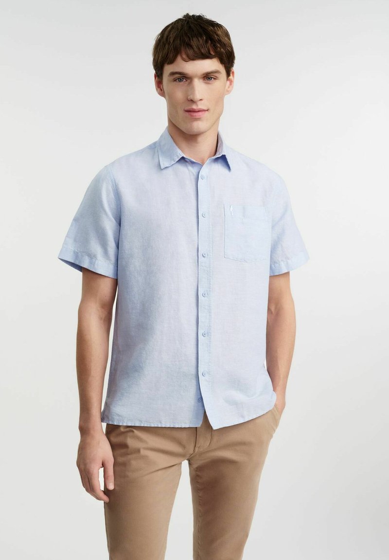Koszula z krótkim rękawem, jasnoniebieska, zapinana na guziki, wykonana z przewiewnego materiału, z kieszonką na piersi i luźnym krojem.