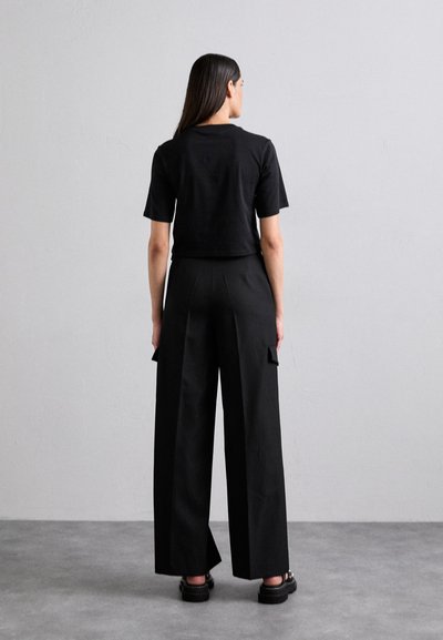 Black cropped t-shirt paired with high-waisted black wide-leg trousers featuring side pockets. Smooth fabric with a matte finish.
