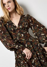 Abito a maniche lunghe con scollatura a V profonda, caratterizzato da un motivo geometrico multicolore in tonalità terrose su uno sfondo scuro. Tessuto fluido e design avvolgente.