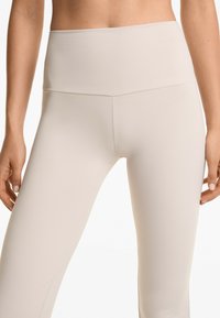 Beige högmidjade leggings tillverkade av slät, stretchig tyg. Har en platt sömdesign, åtsittande form och en minimalistisk stil.