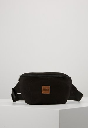 Schwarze Canvas Bauchtasche mit einem Reißverschluss, verstellbarem Tragegurt und einem Logo-Patch aus braunem Leder. Rechteckige Form mit einer strukturierten Oberfläche.
