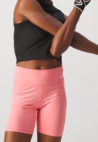 Pantalones cortos deportivos de tiro alto en color rosa, hechos de un tejido elástico, con una textura suave y un pequeño logo blanco en la cinturilla.