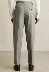 Gray wool trousers with a flat front, soft texture, side adjusters, and back pockets, finished with cuffed hems and black loafers.