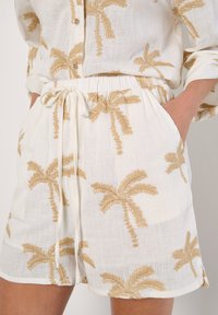 Vita shorts med guld palmträd broderi, elastisk midja, dragsko stängning, mjuk linnetextur och sidofickor.
