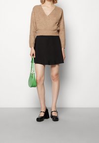 Pull en khaki noué, jupe évasée noire, sac à main vert et chaussures Mary Jane à plateforme noires. Texture douce et détails de design simples.