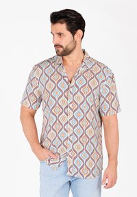 Camisa de manga corta en una tela ligera con un patrón de olas multicolores en tonos azul, naranja y crema. Diseño de botones.