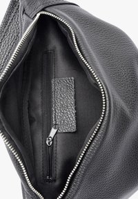 Interno di una borsa in pelle nera con tasca con zip, fodera liscia, etichetta testurizzata e dettagli in cerniera argentata lungo il bordo.