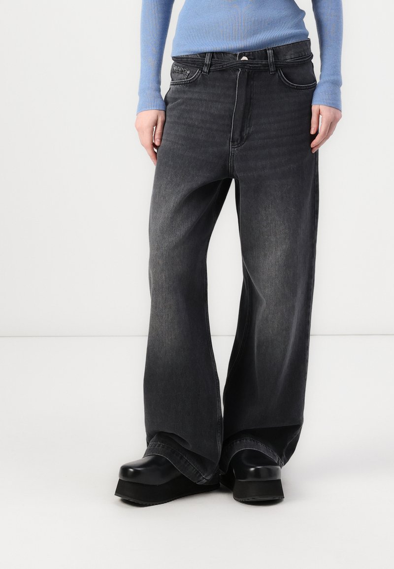 Wide-leg black denim jeans with subtle fading, five-pocket design, and stitching details. Worn with black platform shoes and a light blue top.