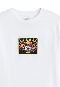 T-shirt bianca in cotone con una colorata toppa grafica raffigurante un volto sorridente, dettagli gialli e uno sfondo nero a raggi di sole.