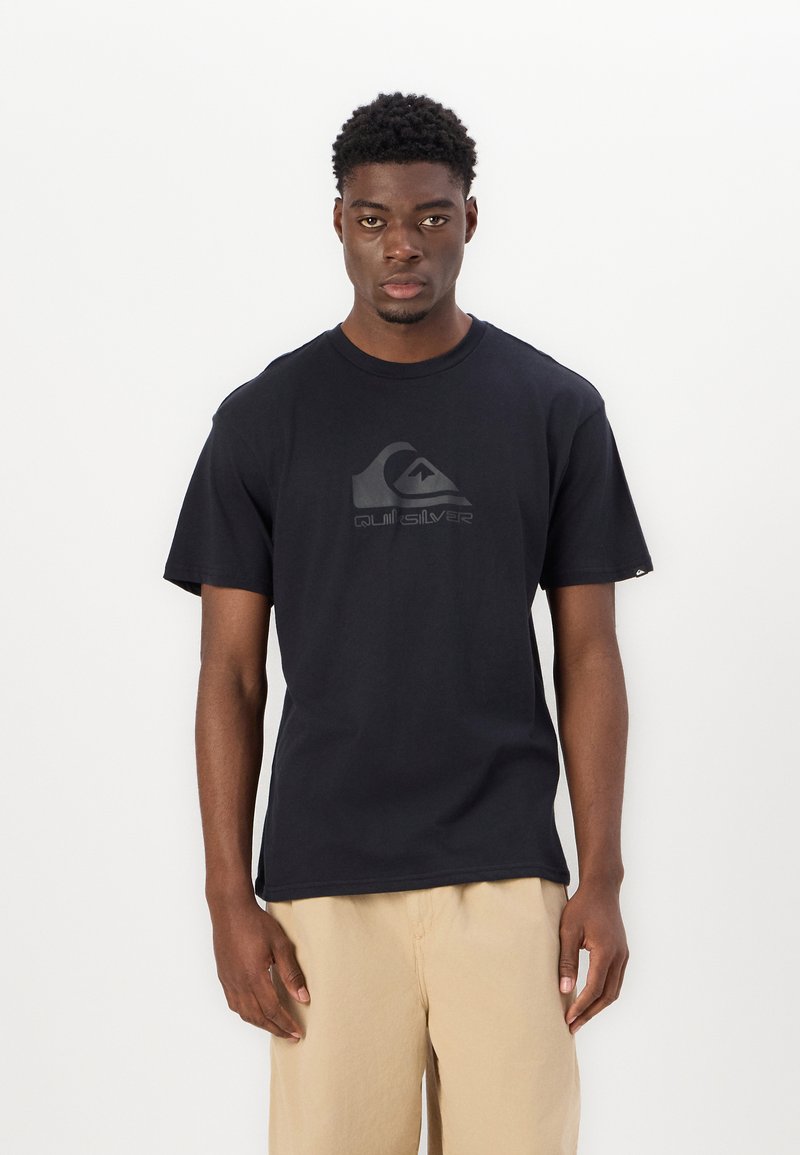 Black cotton t-shirt with a crew neck and short sleeves, featuring a textured gray logo in the center. Worn with beige shorts.