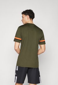 Olijfgroene t-shirt met korte mouwen en zwart-oranje gestreepte accenten op de mouwen, gemaakt van zachte stof, met een ronde hals.