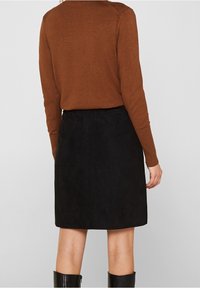 Brauner Pullover kombiniert mit einem schwarzen Wildlederrock. Der Rock ist gerade geschnitten und hat eine glatte Textur, die bis zur Mitte des Oberschenkels reicht.