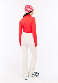 Rode long-sleeve top gecombineerd met witte strakke broek en blauwe skibotten; model draagt een gestreepte rode en witte gebreide muts.