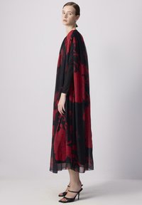 Abito maxi floreale nero con motivi a fiori rossi. Design fluente e tessuto trasparente, completato da una silhouette lunga simile a un mantello.