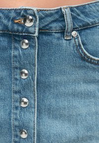 Falda de mezclilla azul claro con cierre frontal de botones, que presenta cinco botones de metal plateado, costuras en contraste y una pretina deshilachada.