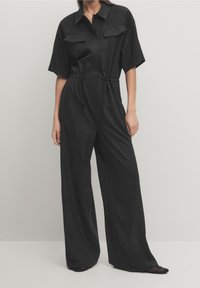 Black jumpsuit made of lightweight fabric, featuring short sleeves, two front pockets, an adjustable drawstring waist, and wide pant legs.
