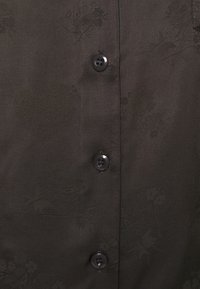 Černá košile s knoflíky a strukturovaným květinovým vzorem, hladká tkanina a čtyři černé knoflíky podél předního zapínání.