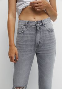 Jean en denim gris avec taille haute, design à cinq poches et détails usés aux genoux. Texture douce et surpiqûres nettes.