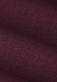 Tissu bordeaux avec une surface texturée, présentant un motif de tissage subtil. Le matériau semble doux et légèrement réfléchissant sous la lumière.