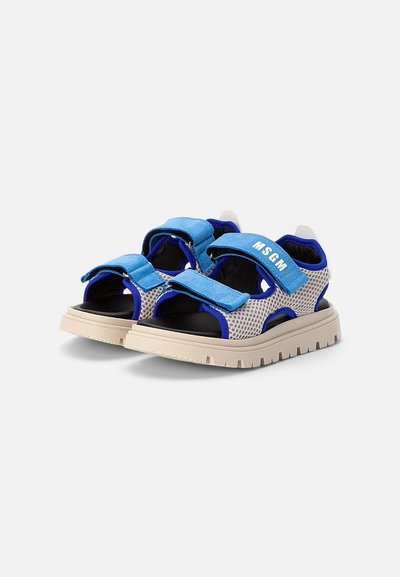 Sandálias de malha com correias de tecido azul e solas de borracha bege. Apresentam fechos ajustáveis de gancho e laço e um design aberto na frente.