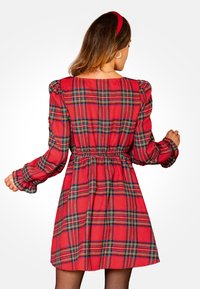 Rode geruite jurk met opgezette mouwen, een cinched taille en een uitlopende rok. Gemaakt van een zachte stof, met groene en zwarte accenten in het patroon.