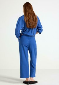 Modrý bavlněný loungewear set zahrnuje volně střiženou mikinu s dlouhým rukávem a kalhoty s širokými nohavicemi, s elastickým pasem a uvolněným střihem.