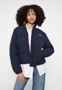 Tumši zila pūšanas jaka ar izšūtu rakstu, rāvējslēdzēja priekšpusi un sānu kabatām. Kreisajā krūtīs ir logotipa uzlikta plāksne un augsta apkakle.