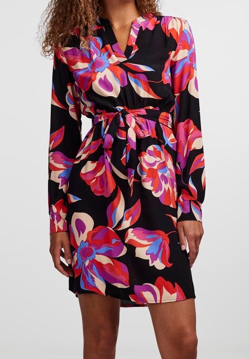 Robe noire à fleurs, dotée de manches longues, d'un col en V et d'une ceinture à nouer. Le motif comprend des fleurs rouges, roses et bleues éclatantes sur un fond sombre.
