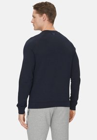 Felpa blu navy con polsini e orlo a costine. Design semplice, tessuto morbido e piccolo logo sul collo. Indossata con pantaloni della tuta grigi.