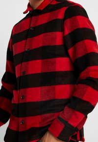 Röd och svart rutmönstrad flanellskjorta med knappstängning fram, krage och långa ärmar i ett mjukt, texturerat tyg.