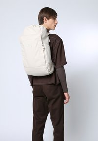 Hellbeige Rucksack mit einem Kordelzugverschluss, einer Reißverschlusstasche und einem minimalistischen Design. Glatte Textur und dezente Farbakzente.