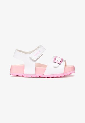 Sandale pour enfant blanche et rose avec bride de cheville réglable et boucle rose à l'avant, semelle rose texturée.