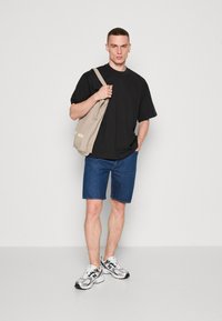 Tricou negru, pantaloni scurți din denim albastru și adidași argintii/albi. Ținând o geantă de umăr bej cu „MS” imprimat. Mâneci scurte și croială lejeră.