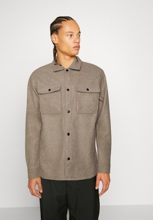 Camisa chaqueta de mezcla de lana marrón con mangas largas, parte delantera abotonada, dos bolsillos de pecho y cuello. Botones negros y diseño discreto.