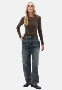 Donkergroene lange mouwen top met kantdetails, gecombineerd met losse, lichtgewassen, high-waisted jeans. Zwarte loafers maken de outfit compleet.