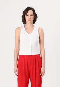 Top sin mangas blanco con textura acanalada, con un escote redondeado y cierre de botones en la parte delantera, combinado con pantalones rojos de cintura alta.