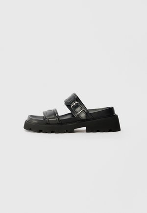 Sort læder slide sandal med en chunky sål, der har to brede stropper og et metalspænde. Struktureret overflade og rillet ydersål.