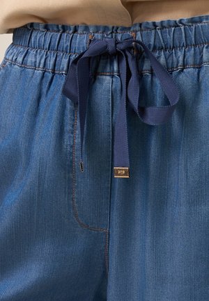 Blue denim pants with an elastic waistband and navy tie detail, featuring vertical stripes and a small metallic brand tag.