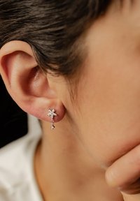 Orecchini in argento a forma di fiore con pietre pendenti, caratterizzati da una finitura lucida e da dettagli intricati su ogni petalo.