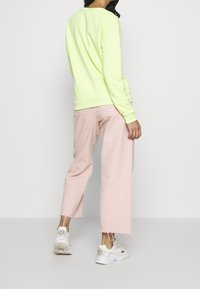 Felpa giallo neon abbinata a pantaloni rosa chiaro a gamba larga e sneakers bianche. La felpa presenta una scollatura rotonda e polsini a coste.